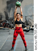 Vertical frontal portrait of a woman lifting a kettlebell standing in a cross training gym. Woman lifting a kettlebell standing in a cross training gym. Стоковое фото, агентство Ingram Publishing / Фотобанк Лори