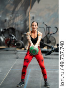 Vertical photo of a mature sportive woman performing kettlebell swing exercise in a gym. Woman performing kettlebell swing exercise in a gym. Стоковое фото, агентство Ingram Publishing / Фотобанк Лори