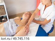 Crop physiotherapist in white uniform holding shoulder and stretching neck of patient lying in bed and closing eyes during massage procedure. Osteopath stretching neck of client during treatment. Стоковое фото, агентство Ingram Publishing / Фотобанк Лори