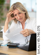 confused worried woman looks through papers sitting at home. Стоковое фото, агентство Ingram Publishing / Фотобанк Лори