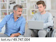 Young man in wheelchair holding laptop, older man looking on. Стоковое фото, агентство Ingram Publishing / Фотобанк Лори