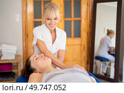 Positive female osteopath in uniform manipulating head of patient lying on couch during psychotherapy session in physical therapy clinic. Smiling physiotherapist treating patient in hospital room. Стоковое фото, агентство Ingram Publishing / Фотобанк Лори