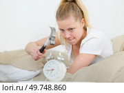 woman in bed ready to crash alarm clock with hammer. Стоковое фото, агентство Ingram Publishing / Фотобанк Лори