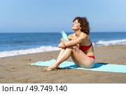 Full body of female traveler in bikini holding bottle with beverage while sunbathing on sandy beach and resting on summer vacation. Slim woman relaxing on seacoast. Стоковое фото, агентство Ingram Publishing / Фотобанк Лори