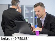 Suited man using laptop next to vending machine. Стоковое фото, агентство Ingram Publishing / Фотобанк Лори