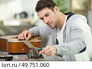 luthier tune guitar strings with peg winder. Стоковое фото, агентство Ingram Publishing / Фотобанк Лори