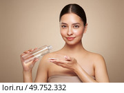 Smiling woman holds bottle with cosmetic tonic. Photo of attractive woman with perfect makeup on beige background. Beauty and skin care concept. Removing makeup. Стоковое фото, агентство Ingram Publishing / Фотобанк Лори