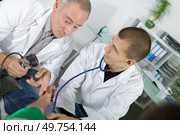 doctor in scrubs taking the blood pressure of a patient. Стоковое фото, агентство Ingram Publishing / Фотобанк Лори