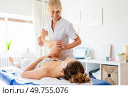 Cheerful female physiotherapist doing osteopathy treatment on leg of patient in light clinic room during rehabilitation session. Smiling osteopath treating woman lying on couch. Стоковое фото, агентство Ingram Publishing / Фотобанк Лори