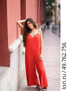 In a vibrant urban setting, a stylish woman in a flowing red jumpsuit poses elegantly, exuding charm and sophistication, attracting the admiration of curious onlookers who admire her fashion sense. An Elegant Woman Dressed in a Stunning Red Jumpsuit Posing Gracefully Against a City Wall. Стоковое фото, агентство Ingram Publishing / Фотобанк Лори