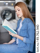 young woman reading a book in laundromat. Стоковое фото, агентство Ingram Publishing / Фотобанк Лори