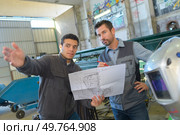 two male engineers in discussion while holding scale drawings. Стоковое фото, агентство Ingram Publishing / Фотобанк Лори