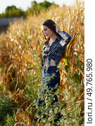 A young woman stands with grace and poise among the vibrant golden corn stalks, dressed in a very stylish outfit that beautifully captures and showcases the delightful beauty of nature all around her. A Young Woman Posing Elegantly in a Beautiful Golden Cornfield Under the Summer Sunlight. Стоковое фото, агентство Ingram Publishing / Фотобанк Лори