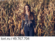 A young woman stands confidently amidst a sprawling cornfield, showcasing her stylish and vibrant outfit while exuding a personality that matches the beauty of the surrounding nature. A young woman in a cornfield shows off her curly hair and stylish outfit with confidence. Стоковое фото, агентство Ingram Publishing / Фотобанк Лори