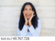 A joyful young woman with curly hair exclaims with excitement, showcasing her happiness against a neutral backdrop that highlights her vibrant personality and fills the air with warmth. An Excited Young Woman with Beautiful Curly Hair Expressing Joy and Enthusiasm Clearly. Стоковое фото, агентство Ingram Publishing / Фотобанк Лори