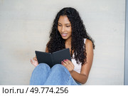 In her inviting and cozy home, a young woman with lovely curly hair and a warm smile happily finds joy while reading on her tablet, creating a peaceful and inviting atmosphere throughout the room. A Young Woman Deeply Engrossed in Reading on Her Tablet While Relaxing at Home Comfortably. Стоковое фото, агентство Ingram Publishing / Фотобанк Лори