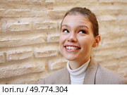 A joyful young woman, radiating happiness with her bright and warm smile, is beautifully captured in a candid moment against a rugged, textured stone wall that adds depth to the scene. A cheerful and youthful young woman is smiling brightly against a beautifully textured wall. Стоковое фото, агентство Ingram Publishing / Фотобанк Лори