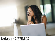 In a bright, contemporary workspace, a young woman with curly hair and stylish glasses focuses intently on her laptop, absorbed in her tasks while considering her next strategic move and future plans. A Thoughtful and Contemplative Young Woman Engaged in Working on a Laptop in a Modern Workspace. Стоковое фото, агентство Ingram Publishing / Фотобанк Лори