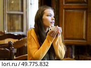 A thoughtful young woman sits in a warm caf, holding a cup of coffee, lost in contemplation, surrounded by rustic charm. Contemplative Young Woman Enjoying Coffee in Cozy Caf. Стоковое фото, агентство Ingram Publishing / Фотобанк Лори