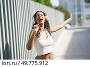 A vibrant and energetic young woman is fully immersed in her music, joyfully singing and dancing outdoors while wearing headphones on a beautiful, sunny day filled with warmth and light. A Joyful Young Woman Singing and Dancing with Headphones While Enjoying the Outdoors. Стоковое фото, агентство Ingram Publishing / Фотобанк Лори