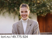 A vibrant young woman radiates confidence and warmth while smiling at the camera, dressed in a stylish blazer and cozy turtleneck, amidst a beautiful backdrop of greenery and sunlight. Confident young woman smiling outdoors in stylish blazer, radiating joy and positivity. Стоковое фото, агентство Ingram Publishing / Фотобанк Лори