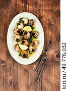 Preparing French Escargot Snails with Herb Butter on wooden rustic background.. Baked snails in sauce, snail butter. Стоковое фото, агентство Ingram Publishing / Фотобанк Лори