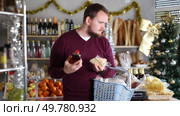 Man is interested in choosing cheese and whiskey in a supermarket decorated for Christmas. Buyer chooses alcohol and snacks. Стоковое видео, видеограф Яков Филимонов / Фотобанк Лори
