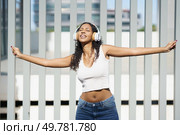 A carefree young woman dances joyfully outdoors in the sunshine, wearing stylish headphones and fully embracing the music, twirling with open arms, feeling the pure essence of freedom and fun. A Joyful Young Woman Expressively Dancing with Headphones in a Vibrant Outdoor Setting. Стоковое фото, агентство Ingram Publishing / Фотобанк Лори
