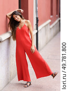 An incredibly fashionable woman proudly wearing a vibrant red jumpsuit strikes a confident pose against a strikingly colorful wall, showcasing her stylish outfit and unique beauty without hesitation. An Elegant Woman in a Stunning Red Jumpsuit is Gracefully Posing Outdoors in Nature. Стоковое фото, агентство Ingram Publishing / Фотобанк Лори