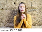 A young woman wearing a vibrant yellow sweater gazes thoughtfully upwards, her expression conveying a mixture of curiosity and hope, lost in her daydreams while leaning against a textured stone wall. A Thoughtful Young Woman Dressed in a Yellow Sweater Relaxing Against a Stone Wall. Стоковое фото, агентство Ingram Publishing / Фотобанк Лори