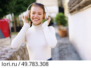 A cheerful young woman listens to music outdoors, wearing stylish headphones. Her joyful expression reflects a moment of happiness and freedom. A Joyful Young Woman is Enjoying Her Favorite Music Outdoors While Wearing Headphones. Стоковое фото, агентство Ingram Publishing / Фотобанк Лори
