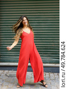A joyful and spirited woman wearing a bright red jumpsuit strikes an exciting and fun dance pose against a vibrant green backdrop, showcasing her lively personality, fashionable style, and energy. A vibrant red jumpsuit featuring a dynamic dance pose set against a lively green background. Стоковое фото, агентство Ingram Publishing / Фотобанк Лори