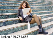 A young woman sits on outdoor stairs, engrossed in a captivating book, dressed stylishly, holding a trendy water bottle, embodying a fashionable casual lifestyle many aspire to emulate. A Relaxed Young Adult Enjoys Reading on the Stairs with a Modern and Stylish Design. Стоковое фото, агентство Ingram Publishing / Фотобанк Лори