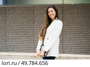 A vibrant young woman, enjoying the outdoors, radiates positivity. She smiles in her chic white blazer, showcasing her modern fashion sense and professionalism with style and confidence. A Confident and Stylish Young Woman is Posing Outdoors while Wearing a Chic Blazer. Стоковое фото, агентство Ingram Publishing / Фотобанк Лори
