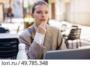 A focused woman in a beige blazer sits outdoors, contemplating while using her laptop in a caf setting. A thoughtful professional woman diligently working outdoors on her laptop, immersed in her tasks. Стоковое фото, агентство Ingram Publishing / Фотобанк Лори