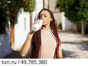 A stylish woman with long braids elegantly sips from a trendy bottle, embracing a vibrant moment in a bustling urban setting, perfect for lifestyle and wellness themes that inspire positivity. A Stylish Young Woman is Happily Enjoying a Refreshing Drink in a Vibrant Urban Setting. Стоковое фото, агентство Ingram Publishing / Фотобанк Лори