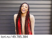 A vibrant and energetic young woman with long, beautifully braided hair adorned with eyecatching red highlights, smiles joyfully and expressively against a richly textured and colorful background. A Joyful Woman with Beautiful Braided Hair Poses Against a Bright Modern Background. Стоковое фото, агентство Ingram Publishing / Фотобанк Лори