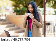 In a serene outdoor workspace, a young woman enjoys sipping her coffee while smiling and engaging with her laptop, surrounded by lush greenery, creating a perfect blend of productivity and relaxation. A woman is enjoying her coffee while diligently working on her laptop outdoors amidst nature. Стоковое фото, агентство Ingram Publishing / Фотобанк Лори