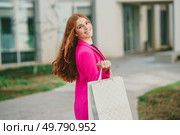 A stylish woman dressed in a vibrant bright pink blazer joyfully carries a shopping bag while outdoors, perfectly embodying the essence of fashion, sophistication, and pure happiness. A Fashionable Young Woman Happily Carrying a Shopping Bag While Enjoying a Day Out. Стоковое фото, агентство Ingram Publishing / Фотобанк Лори
