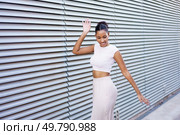 A stylish young woman elegantly strikes a playful pose against a contemporary, textured wall, radiating an infectious blend of confidence and joy while showcasing her unique fashion sense. A Charming Young Woman Posing Delightfully Against a Modern and Stylish Background Environment. Стоковое фото, агентство Ingram Publishing / Фотобанк Лори