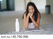 A young woman sits comfortably and smiles while using her laptop in a relaxed atmosphere, elegantly showcasing the blend of modern technology with a casual lifestyle that many aspire to live. A Young Woman Engaged Deeply with Her Laptop While Seated Comfortably in a Casual Setting. Стоковое фото, агентство Ingram Publishing / Фотобанк Лори