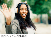 A spirited and lively young woman wearing her stylish headphones joyfully dances outdoors, radiating positivity and abundant happiness as she passionately enjoys listening to her favorite music. A Joyful Young Woman is Delightfully Enjoying Music Outdoors while Wearing Headphones. Стоковое фото, агентство Ingram Publishing / Фотобанк Лори