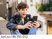 A joyful young person enthusiastically interacts with their smartphone while outdoors, vividly showcasing their excitement and connection in a lively and vibrant urban environment filled with energy. A cheerful young person is happily engaging with their smartphone in a bustling urban environment. Стоковое фото, агентство Ingram Publishing / Фотобанк Лори