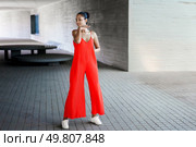 In an urban environment, a stylish and fashionable woman is striking a confident pose while wearing a vibrant red jumpsuit, effectively showcasing her contemporary sense of style and natural grace. A Stylish Woman Dressed in a Bright Red Jumpsuit Gracefully Posing Outdoors in Daylight. Стоковое фото, агентство Ingram Publishing / Фотобанк Лори