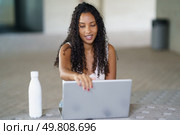 In a vibrant indoor space, a young woman with curly hair is engaged with her modern laptop, showcasing the importance of contemporary work culture and digital interaction in our lives. A Young Woman Fully Engaged with Her Laptop While in a Bright and Spacious Indoor Workspace. Стоковое фото, агентство Ingram Publishing / Фотобанк Лори
