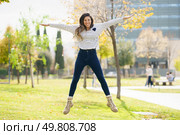 A joyful and happy young woman leaps into the air with her arms fully outstretched in a vibrant, lush park, radiating energy and pure joy while surrounded by the breathtaking beauty of nature. A Joyful Woman is Jumping with Excitement Outdoors in a Beautiful Green Park Setting. Стоковое фото, агентство Ingram Publishing / Фотобанк Лори