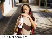 In a vibrant outdoor scene, a young woman with braided hair joyfully holds a refreshing bottle, radiating happiness and confidence, embodying freedom and a spirit of adventure in this perfect moment. A Young Woman is Having Fun and Enjoying Life while Holding a Bottle Outdoors and Smiling. Стоковое фото, агентство Ingram Publishing / Фотобанк Лори