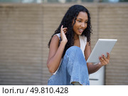 A cheerful and lively young woman beams with joy while engaging in a video chat on her tablet, illustrating a dynamic and enjoyable interaction in a relaxed and casual indoor setting. A young woman joyfully engages in a video call on her tablet, enjoying meaningful connections. Стоковое фото, агентство Ingram Publishing / Фотобанк Лори
