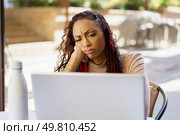 A woman with curly hair and braids looks intently at her laptop, displaying a thoughtful, concerned expression, likely engaged in a challenging task that requires her full attention. A Focused Woman Intently Working on Her Laptop While Exhibiting a Concerned Expression on Her Face. Стоковое фото, агентство Ingram Publishing / Фотобанк Лори