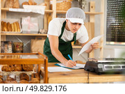 Bakery guy employee in apron examines documents, ponders debt restructuring. Стоковое фото, фотограф Яков Филимонов / Фотобанк Лори